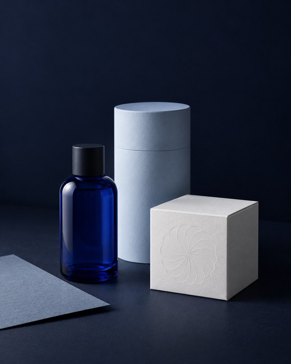 Product concept featuring a cobalt-blue glass bottle, a light-blue cylindrical package and a white box with a rosette embossing.